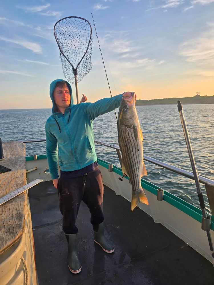 Person in a blue hoodie holds a large fish on a boat, with a fishing net in the background.