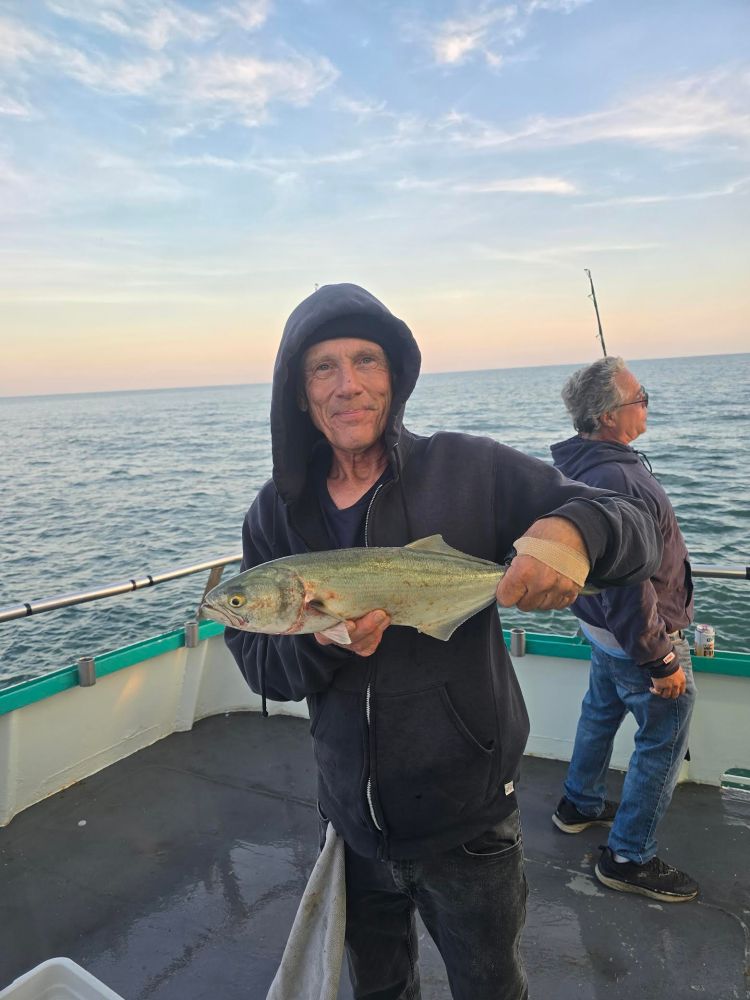 Man in hoodie holding a fish on a boat at sea.