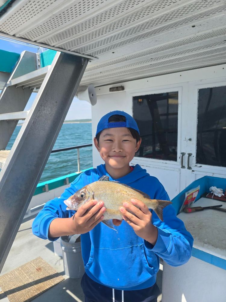 Boy in blue hoodie and cap holds fish on a boat deck.