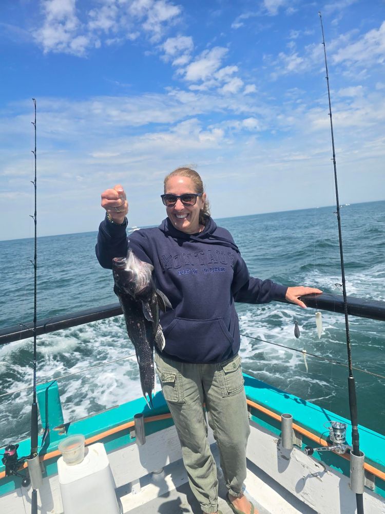 Person on a boat holding a fish, with fishing poles and the ocean in the background.
