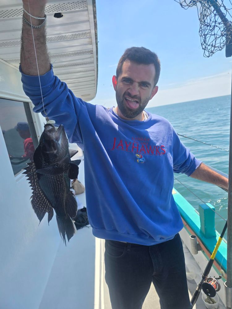 Person on a boat holding up a fish and sticking out tongue.