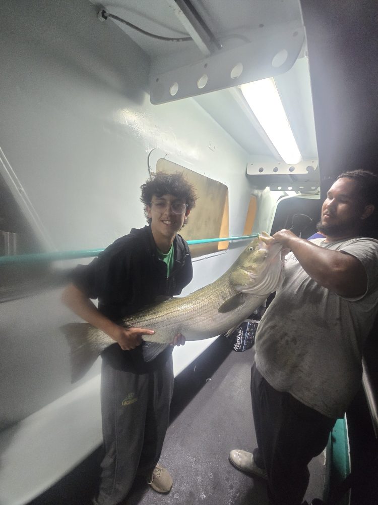 Two people holding a large fish indoors, under bright overhead light.
