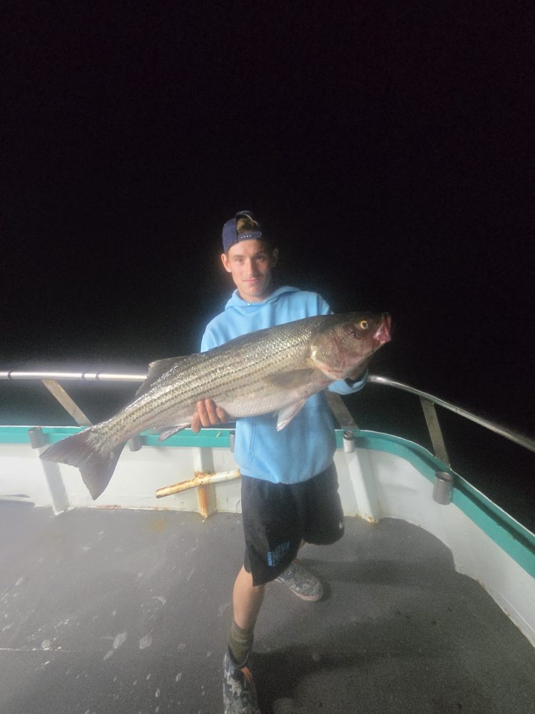 Person holding a large fish on a boat at night.