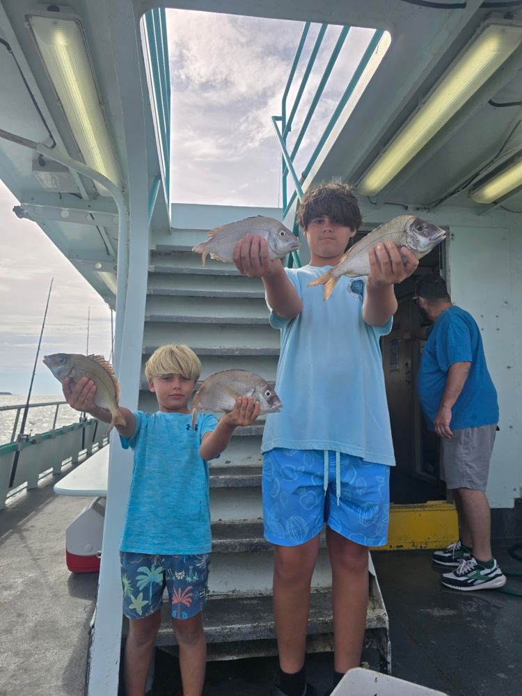 Two kids holding fish on a boat near stairs, with another person in the background.