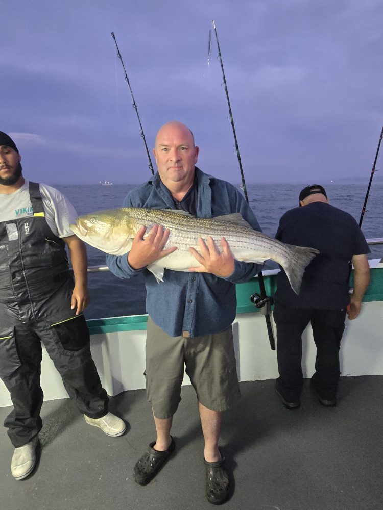 Man holding a large fish on a boat with fishing rods in the background.
