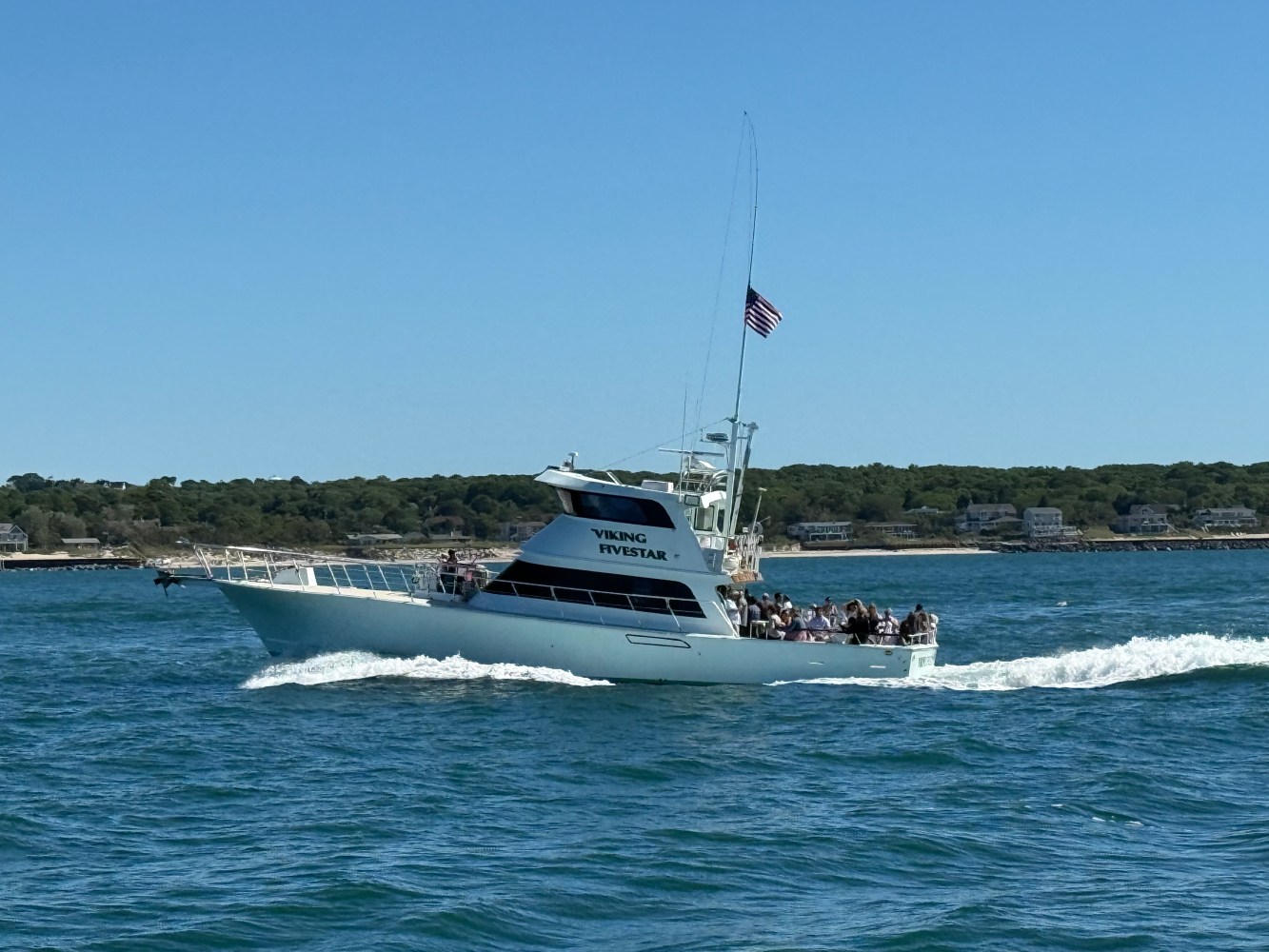 Boat with passengers on water under clear sky, American flag waving.