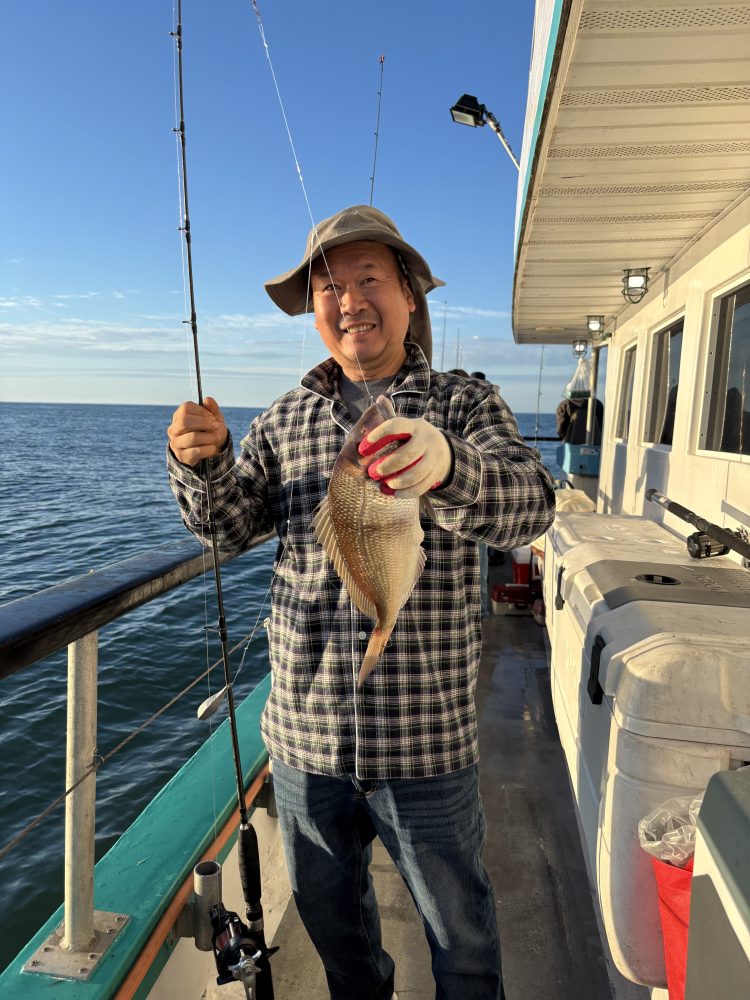 Person on a boat holding a fish with a fishing rod, wearing a hat and plaid shirt.