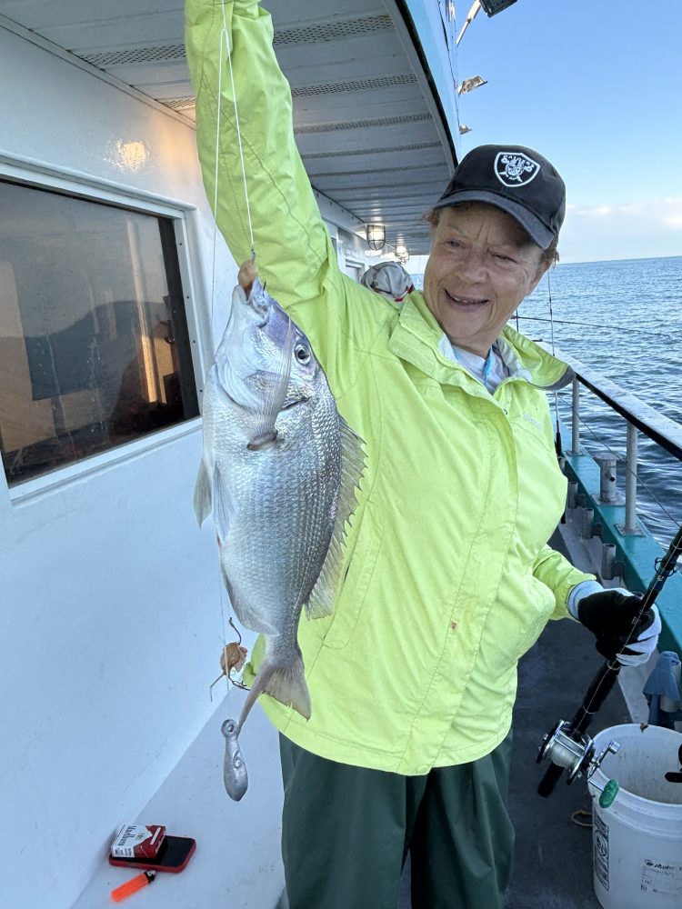 Person in yellow jacket holds a fish on a boat near the shore.