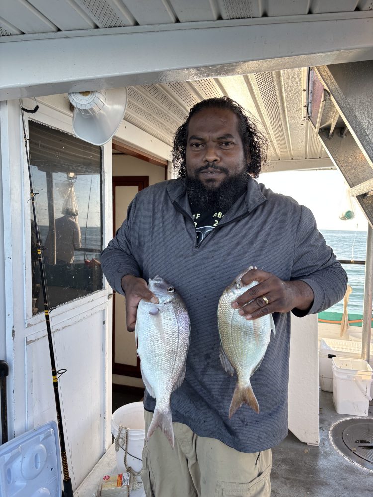 Person holding two fish on a boat interior.