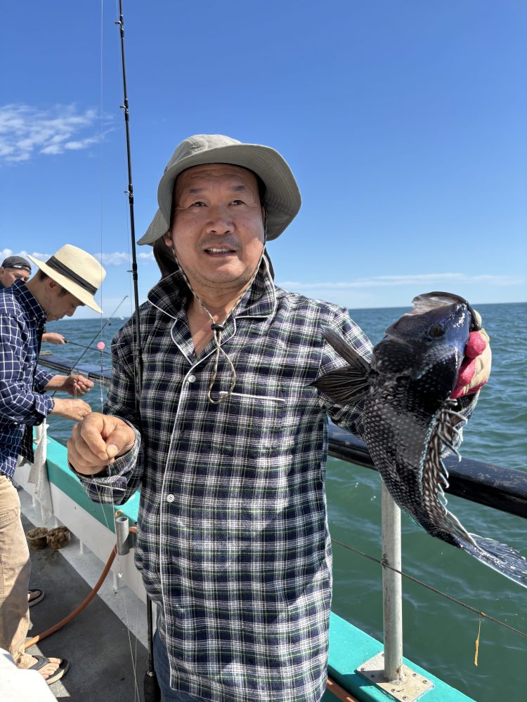 Person on boat holding a fish, wearing a hat and checkered shirt.