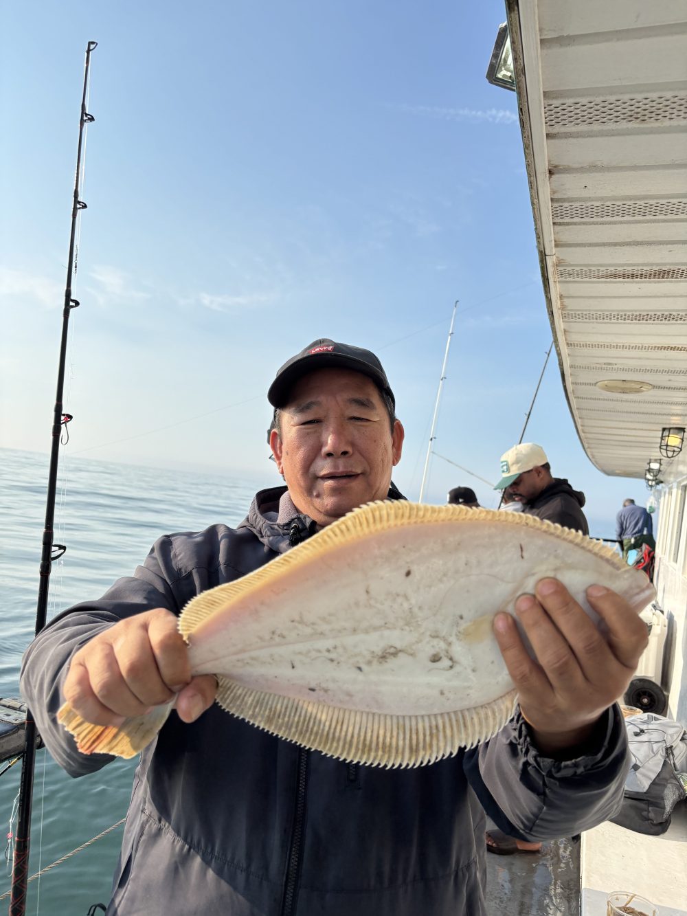Person holding a flat fish on a boat with fishing rods visible.