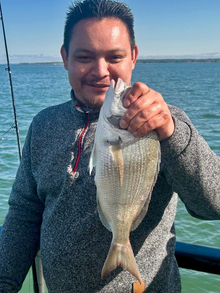 Person holding a fish on a boat with water and sky in the background.
