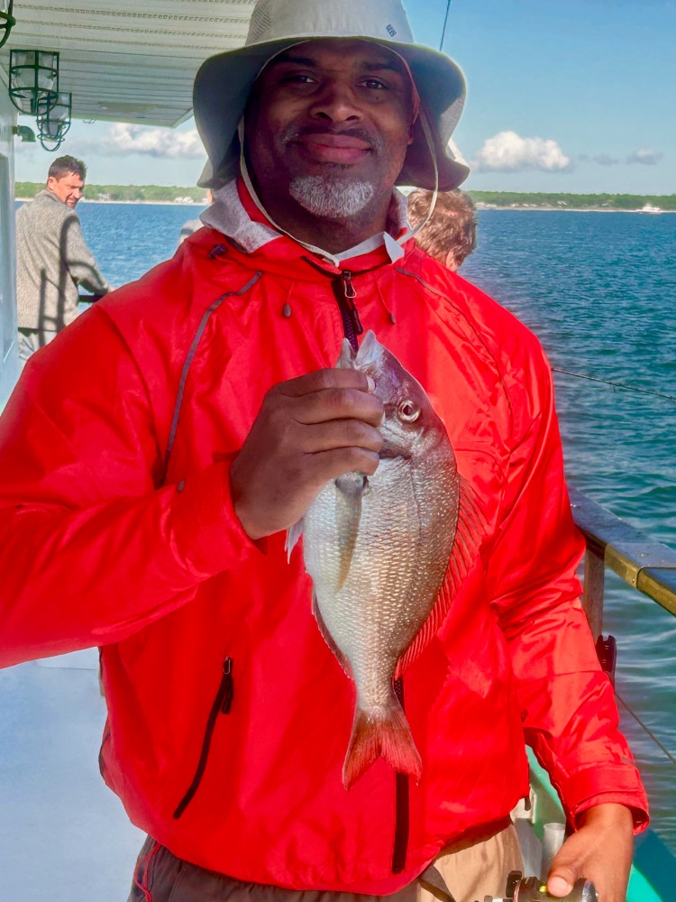 Man in red jacket and hat holding a fish on a boat.