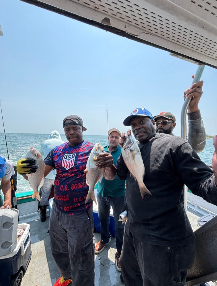 Group of people on a boat holding fish they caught.