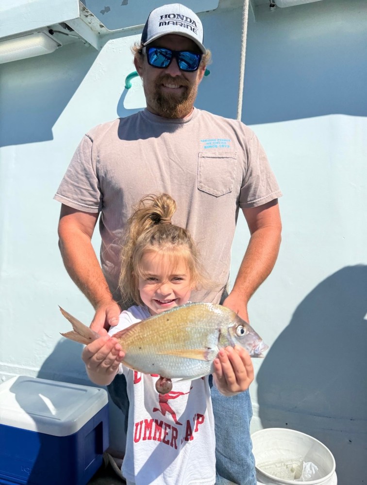 Man and child smiling with fish on boat deck.