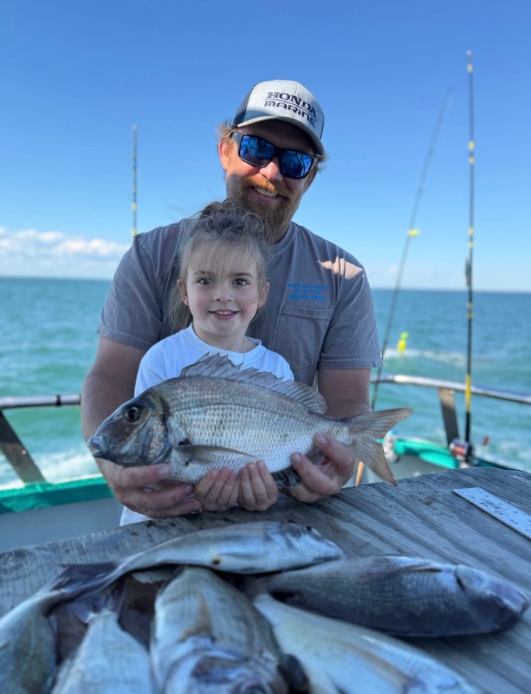 Man and child holding a fish on a boat, with more fish on a table.
