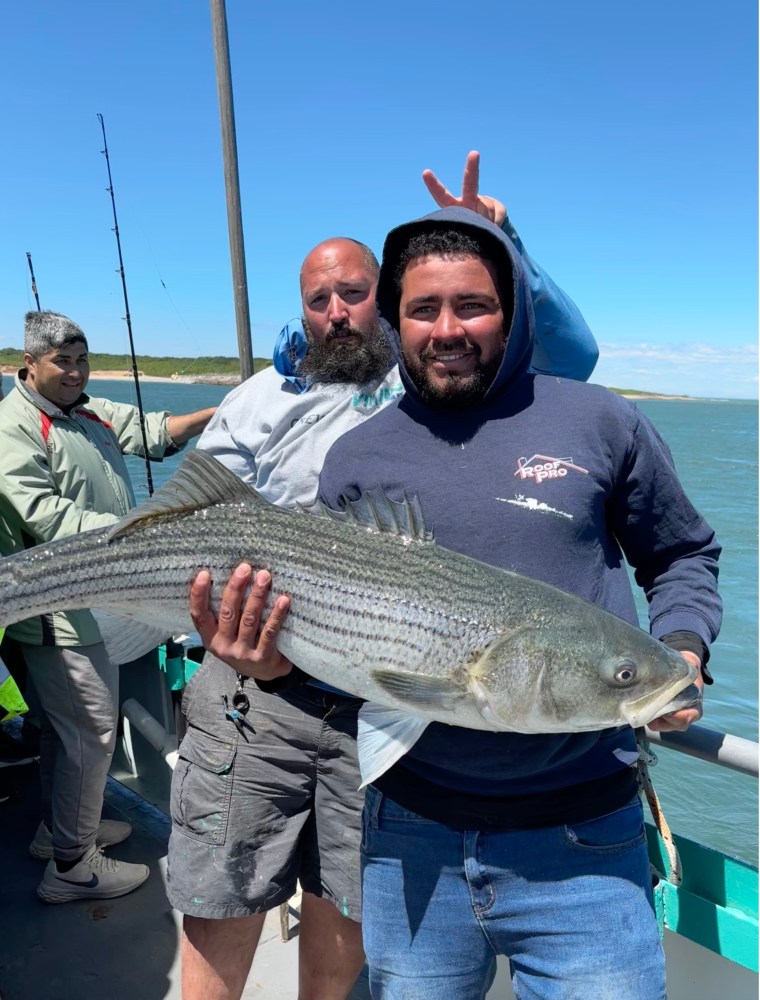 Two men on a boat holding a large fish, with ocean and sky in the background.