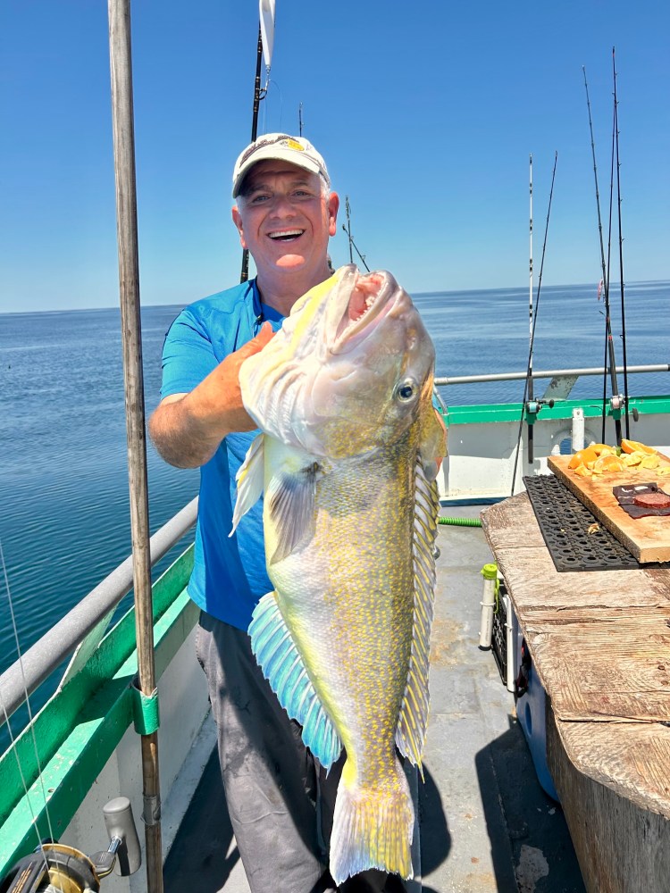 Man holding large fish on a boat at sea under a clear blue sky.
