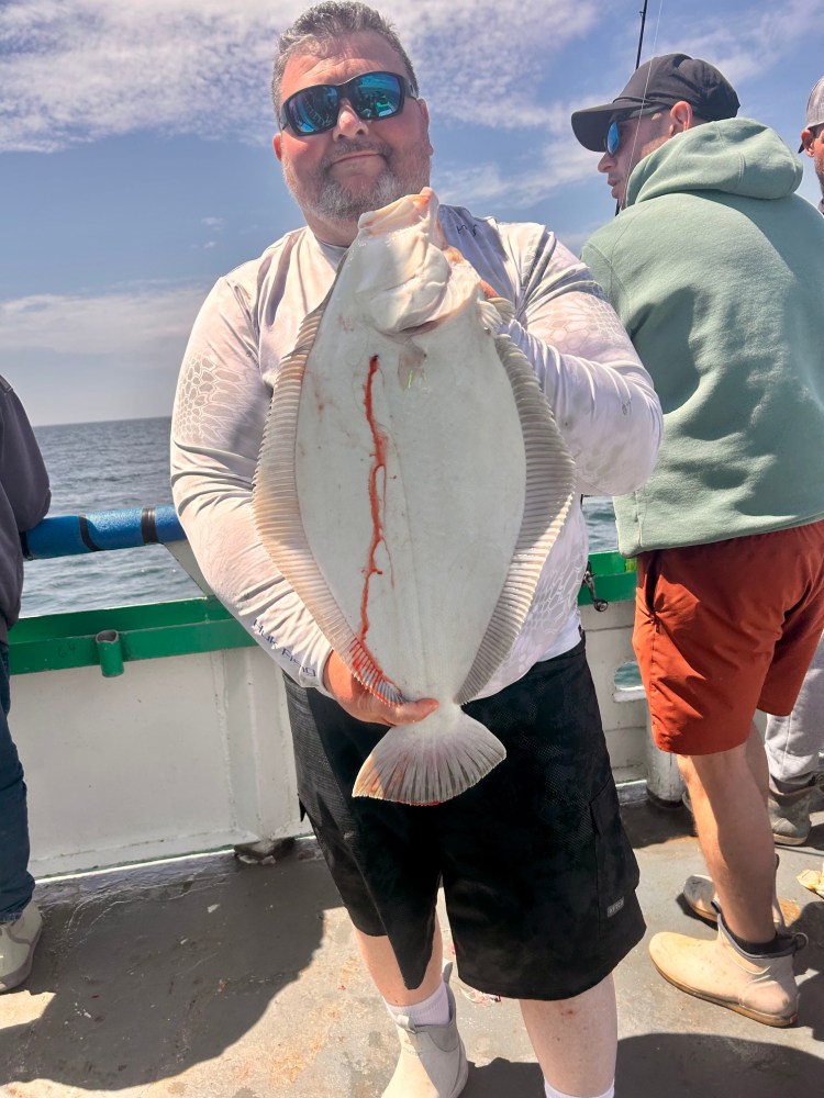 Man holding large fish on a boat under a sunny sky.