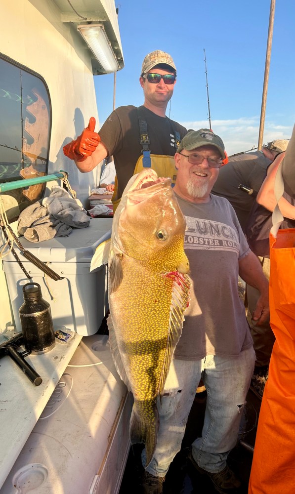Two men on a boat holding a large fish caught during fishing.