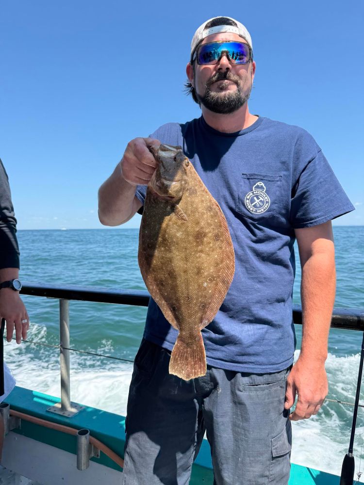 Person holding a fish on a boat under a clear blue sky.