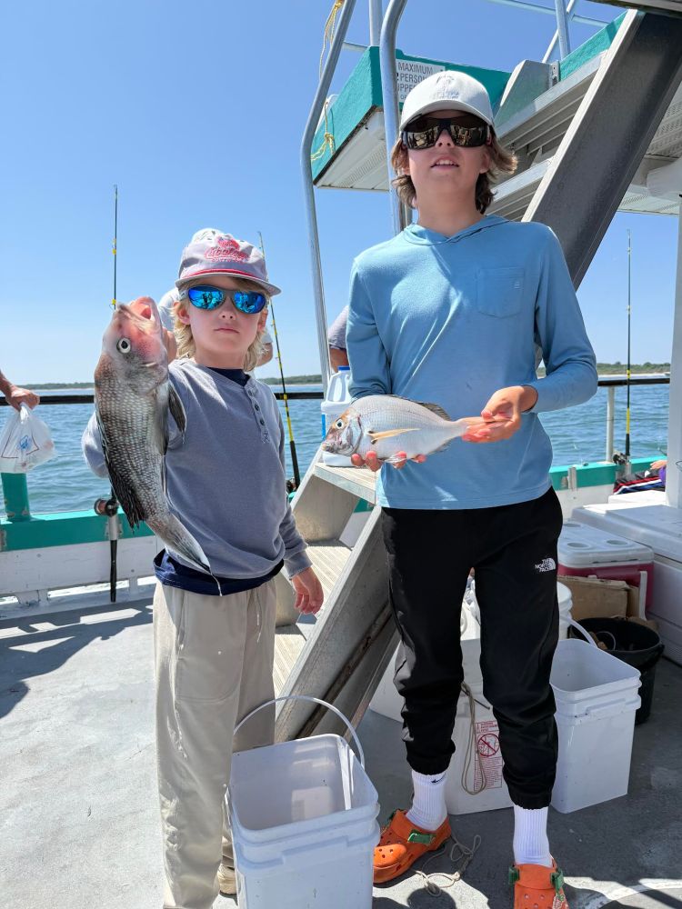 Two kids in caps holding fish on a boat deck.