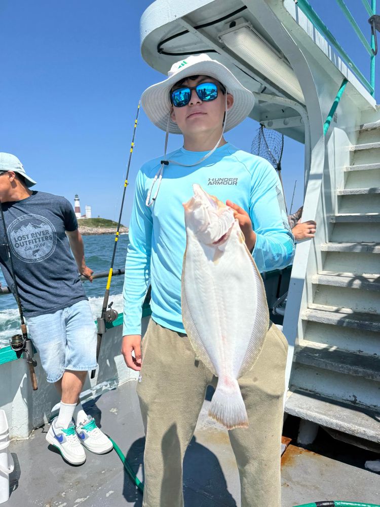 Person on a boat holding a large fish, wearing a hat and sunglasses.