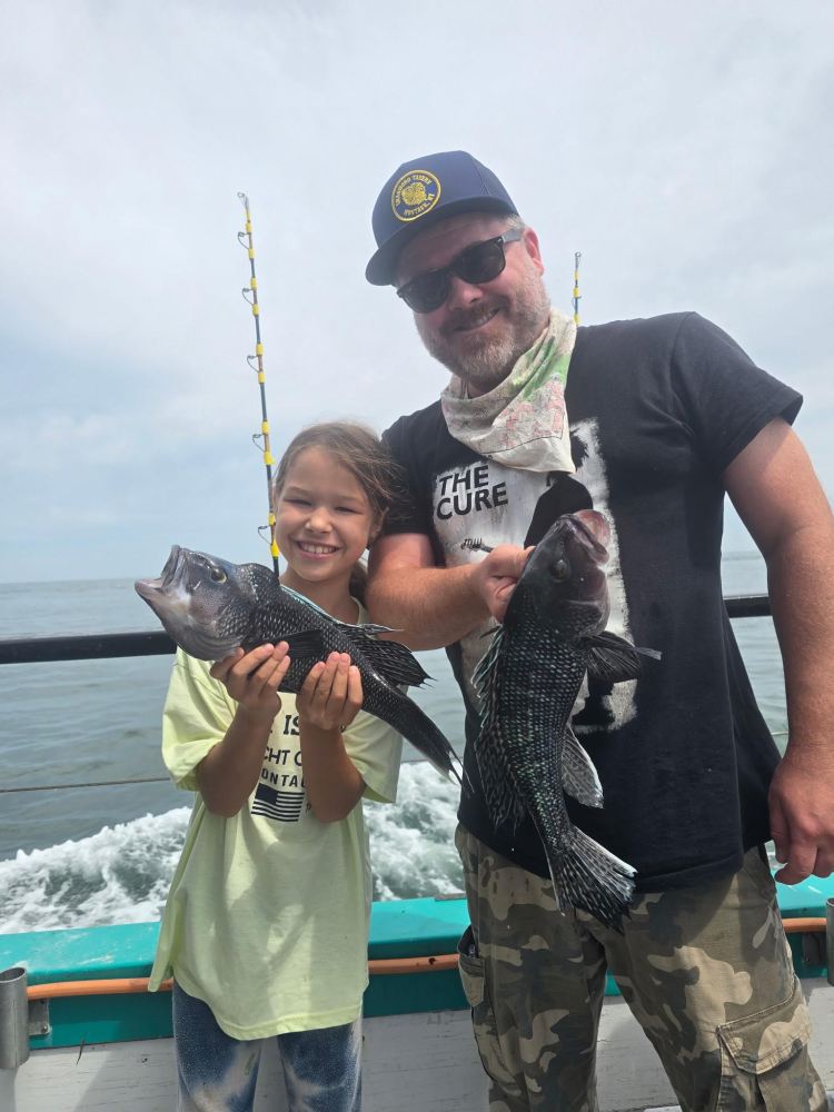 Child and adult holding fish on a boat with ocean in background.