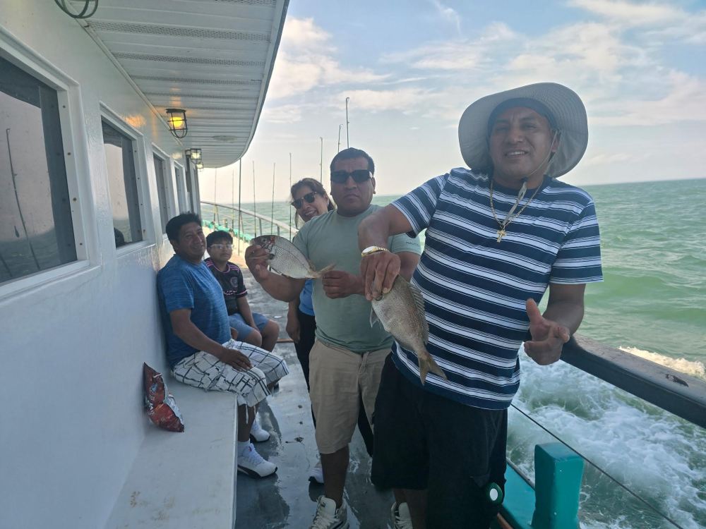 Group of men on a boat holding fish, smiling at the camera.