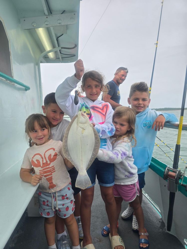 Group of children on a boat holding up a caught fish.