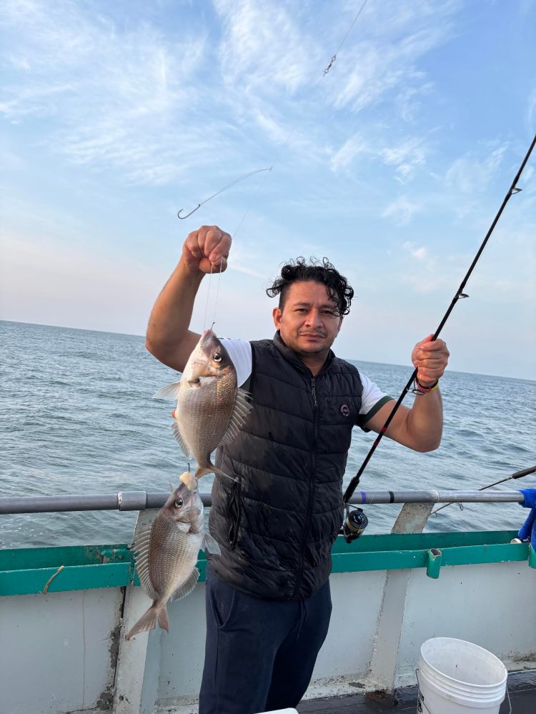 Man holding fishing rod with two fish on a boat over the ocean.