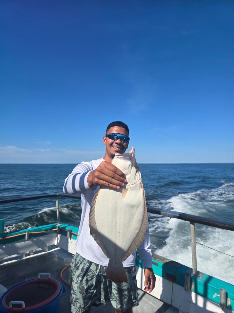 Person on boat holding a large fish, ocean and sky in the background.