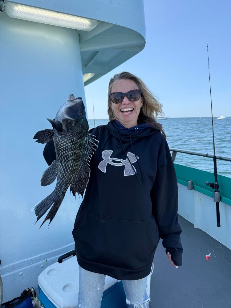 Person smiling, holding a large fish on a boat deck.