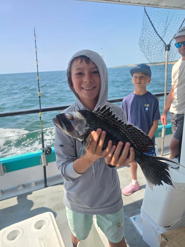 Boy holding a fish on a boat, with another boy and an adult nearby.