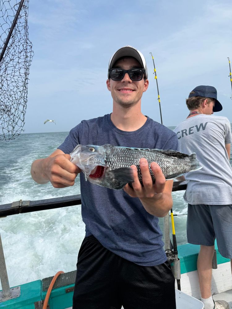 Man holding a fish on a boat, wearing sunglasses and a cap. Another person in the background.