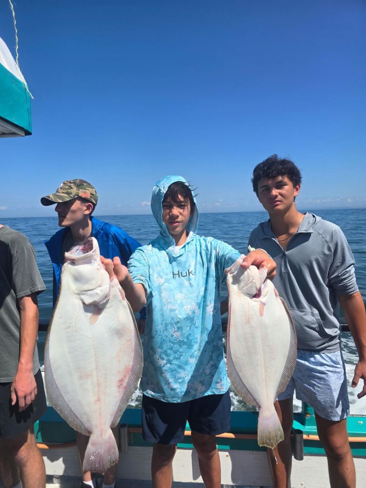 Three young men on a boat holding two large flat fish.