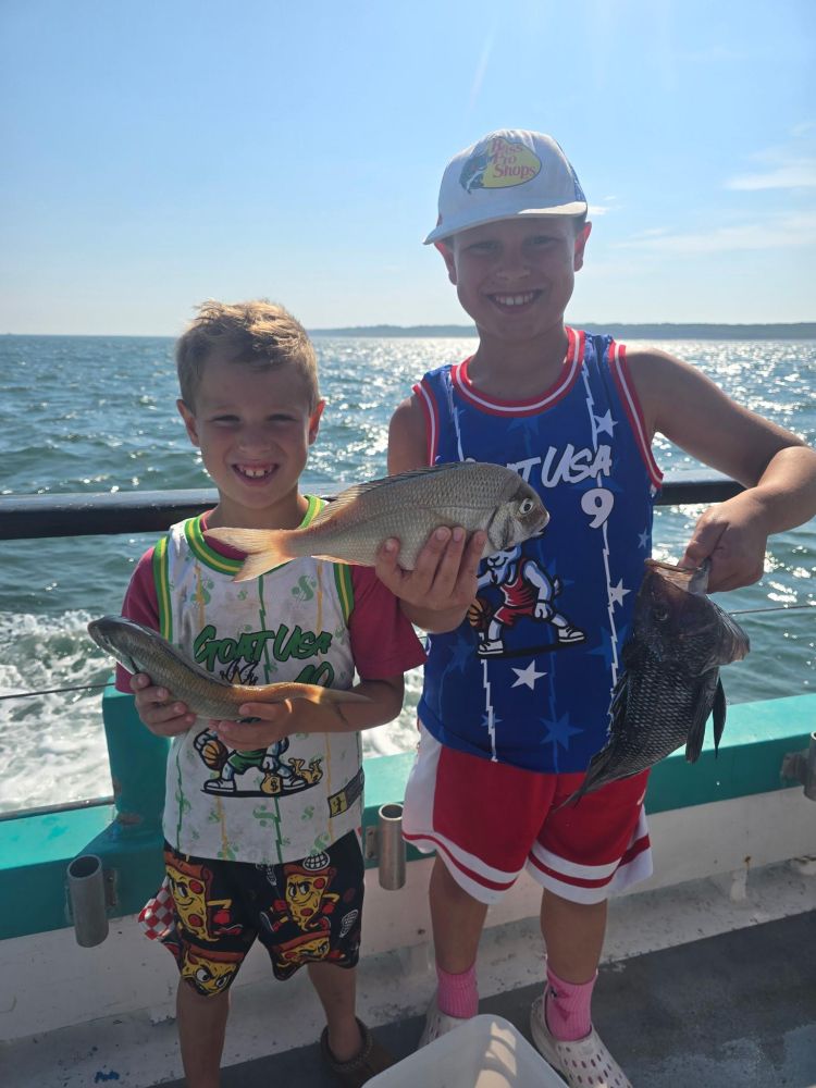 Two smiling children on a boat holding fish they caught.