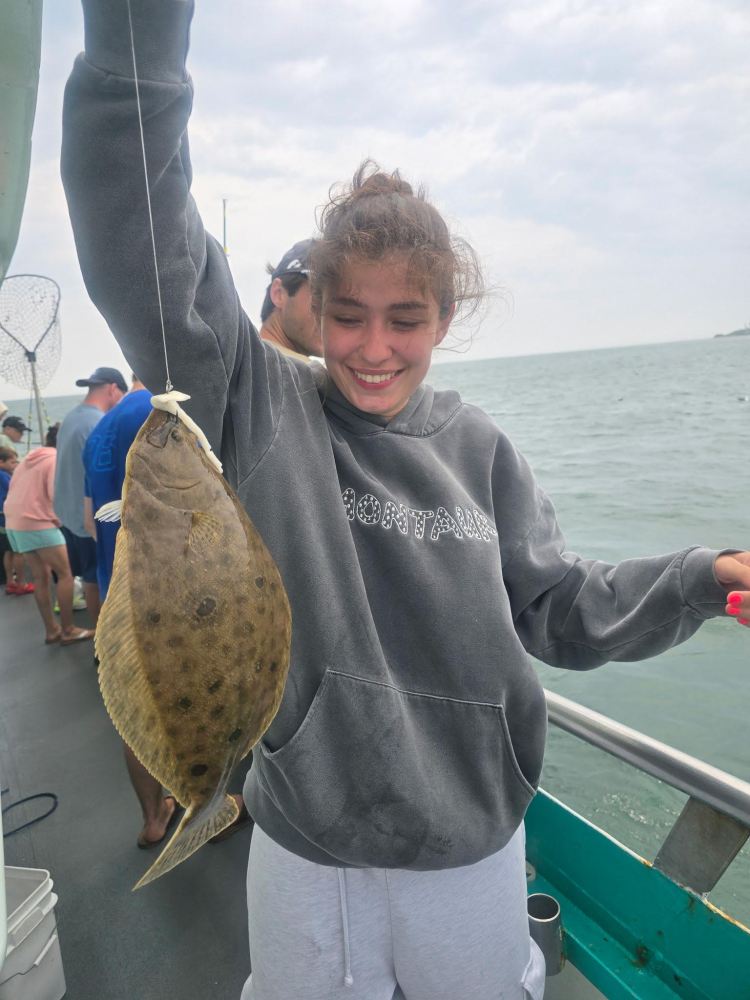Person holding a large flatfish on a boat with ocean background.