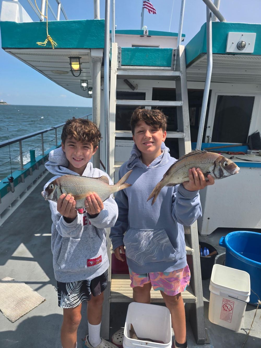 Two boys on a boat holding freshly caught fish, smiling.