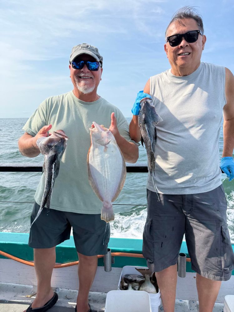 Two men holding fish on a boat with ocean in the background.