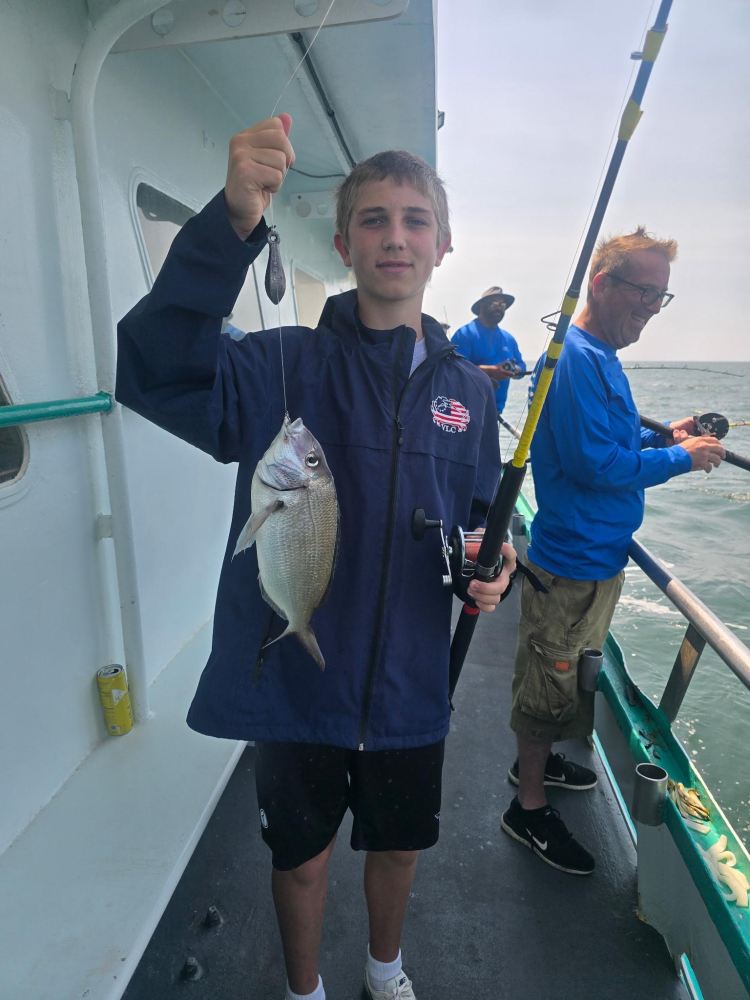 Person holding a fish on a boat while fishing with others.