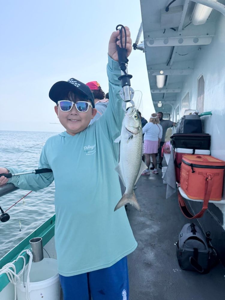 Child smiling, holding a fish on a boat deck.