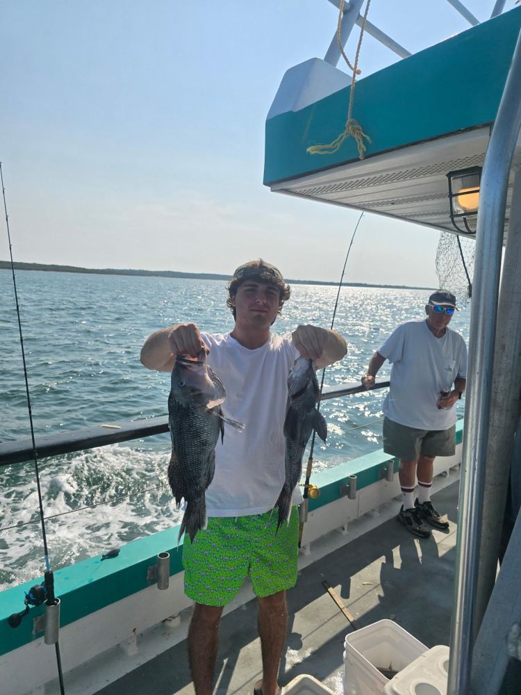 Person on a boat holding two fish with the sea in the background.