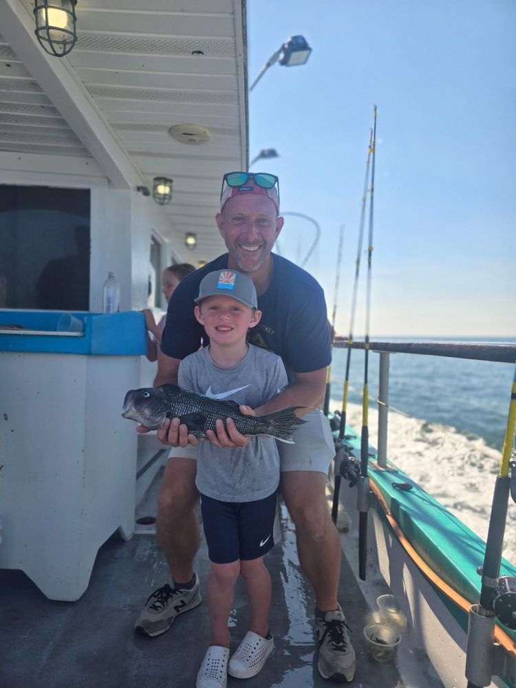 Man and child on a boat holding a fish, smiling at the camera.