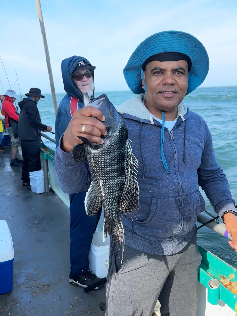 Man in a blue hat holds a fish on a boat with others fishing nearby.