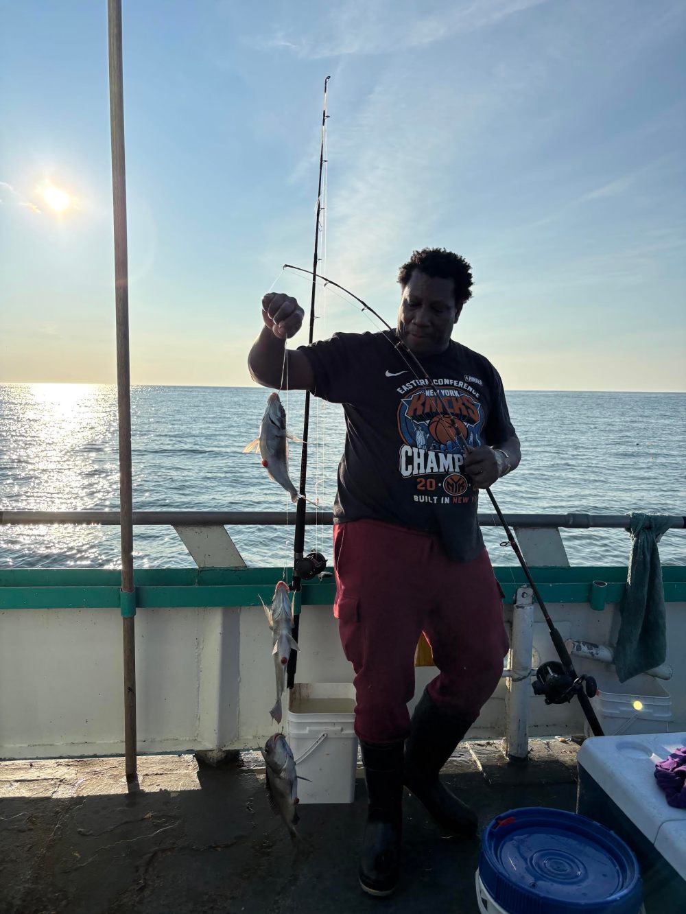 Person on boat holding fishing rod with caught fish, ocean backdrop.