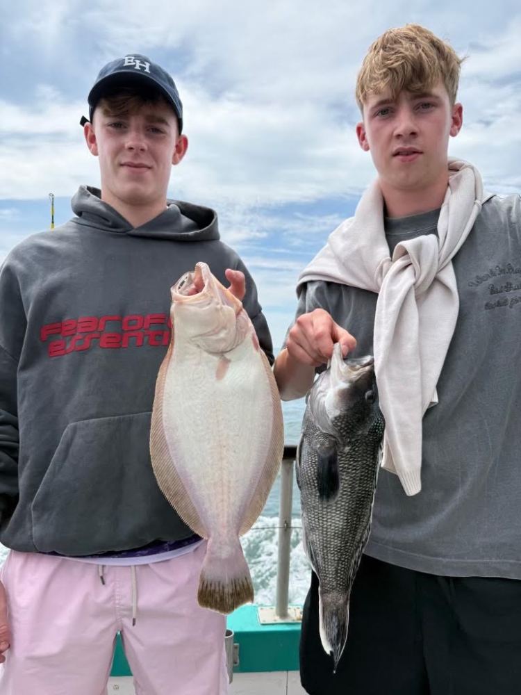 Two young men holding fish on a boat with the ocean in the background.