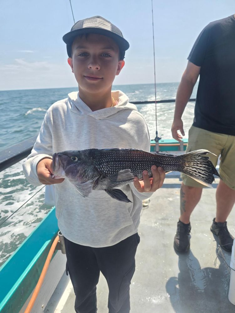 Child holding a fish on a boat with the ocean in the background.