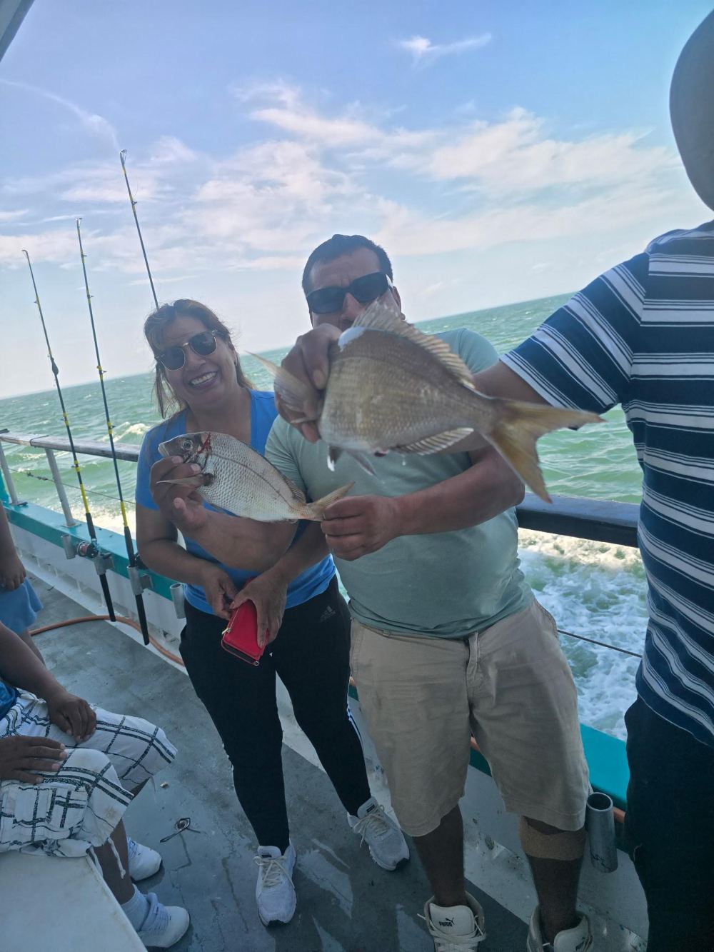 People on a boat holding fish during a sunny day at sea.