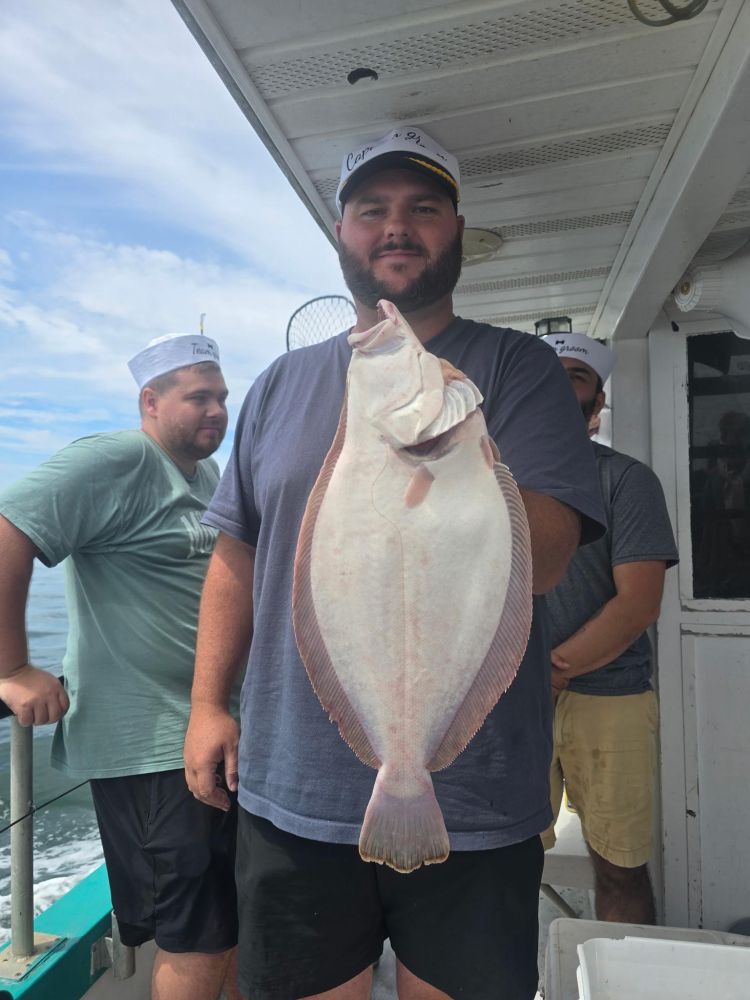 Man on boat holding a large flat fish, two men in the background.